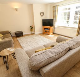 A living room with sofas a television on a wooden stand a rug and a window with curtains at 1 The Stables in Alston