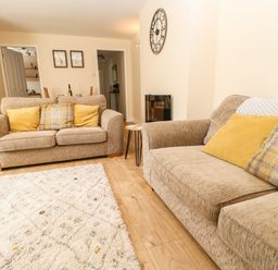 A living room with two beige sofas and yellow cushions a small side table and wall clock at 1 The Stables in Alston