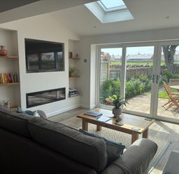 A living room with a television and a sliding door leading to the garden at The Nest in Beadnell