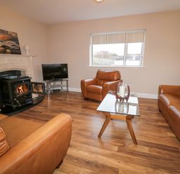 A living room with brown leather sofas a glass coffee table a wood burning stove and a television at Loughanure Lake View in Loughanure County Donegal