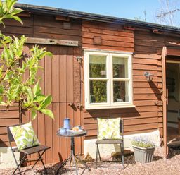 Outdoor seating area with two chairs and a small table in front of a wooden building at The Garden Lodge in Upton Cressett near Bridgnorth