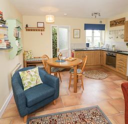 A kitchen and dining area with wooden cabinets a round wooden table four chairs a blue armchair and a red armchair at The Garden Lodge in Upton Cressett near Bridgnorth