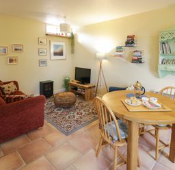 A sitting and dining area with a red sofa a wooden table with chairs a television and wall shelves at The Garden Lodge in Upton Cressett near Bridgnorth