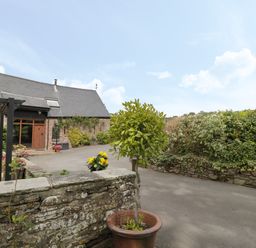 A stone wall with potted plants and a building with slate roof and wooden door at Pentre Barn in Llantilio Pertholey near Mardy