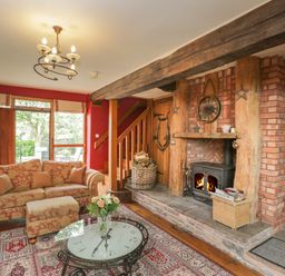 A living room with a sofa ottoman glass coffee table rug fireplace and wooden beams at Pentre Barn in Llantilio Pertholey near Mardy