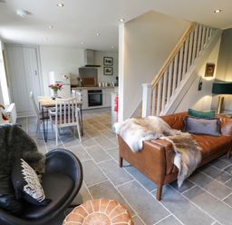 A living area with leather sofas and a black chair next to a dining table and kitchen at Swn yr Afon in Beddgelert