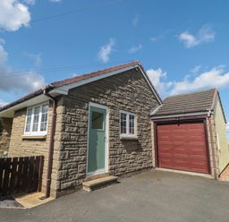 The exterior of a stone house with a green door and a red garage door under a blue sky at Island View Cottage in High Hauxley near Amble