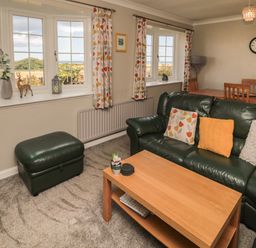 A living room with green leather sofa and ottoman wooden coffee table and dining table by the windows at Island View Cottage in High Hauxley near Amble
