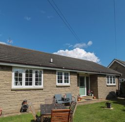 A stone bungalow with white windows and a green door a wooden table and chairs on grass outside Island View Cottage High Hauxley near Amble