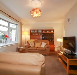A living room with leather sofas a wooden TV stand window with patterned curtains and a wooden cabinet at Garden View in Quintrell Downs near Newquay