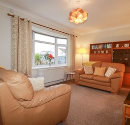 A living room with tan leather sofas and a wooden cabinet at Garden View in Quintrell Downs near Newquay