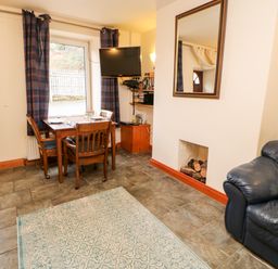 A living room with a dining table by a window a wall-mounted television and leather sofas at Hunter Cottage in Haltwhistle near Hadrians Wall