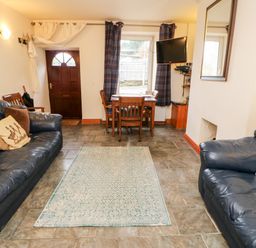 A living room with two leather sofas a dining table with chairs a wall-mounted television and a front door at Hunter Cottage in Haltwhistle near Hadrians Wall