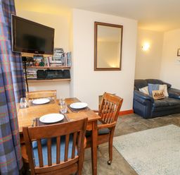 A dining table with four plates and glasses near a wall-mounted TV and shelves with books and a stereo and a small sofa with cushions in a living area at Hunter Cottage in Haltwhistle near Hadrians Wall