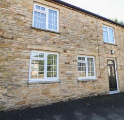 Stone exterior wall of a building with four white windows and a black door at The Forge in Allendale