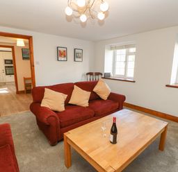 A living room with red sofas a wooden coffee table with a bottle and glass and two windows at The Forge in Allendale