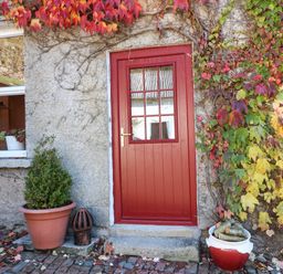 A red door with glass panels surrounded by a stone wall with autumn leaves and potted plants at Carley's Bridge House in Carley's Bridge near Enniscorthy County Wexford