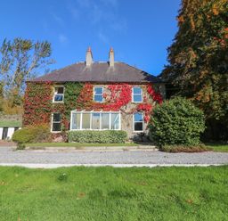 A two-story house with ivy on the walls and a glass porch in front with trees and grass around at Carley's Bridge House in Carley's Bridge near Enniscorthy County Wexford