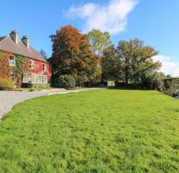 A house with ivy on the walls next to a gravel driveway and green lawn near trees and a river at Carley's Bridge House in Carley's Bridge near Enniscorthy County Wexford