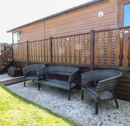 A patio area with outdoor wicker chairs and bench next to a wooden cabin at Doormouse Lodge South Lakeland Leisure Village
