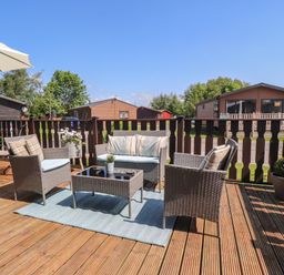 An outdoor deck with wicker chairs a table an umbrella and potted plants at Doormouse Lodge in South Lakeland Leisure Village