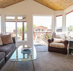 A living room with a sofa and armchair next to a glass coffee table and large windows at Doormouse Lodge in South Lakeland Leisure Village