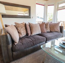 A living room with a dark sofa with multiple pillows a standing lamp a rectangular mirror and a glass coffee table with a tray and remote controls at Doormouse Lodge South Lakeland Leisure Village