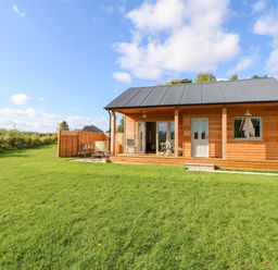 A wooden cabin with a porch and outdoor seating on a grassy lawn at Rising Sun in Kirkbymoorside