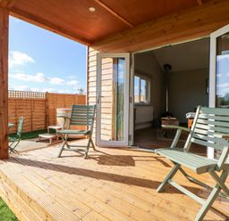 A wooden porch with two chairs and an open door leading to a living room at Rising Sun in Kirkbymoorside