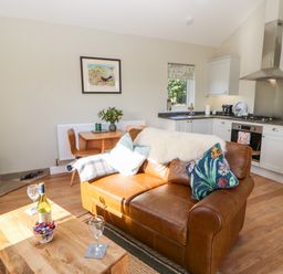 A living room with a leather sofa and wooden coffee table and a kitchen with white cabinets and a stove at Rising Sun in Kirkbymoorside