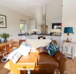 A kitchen and dining area with a brown leather sofa in the foreground a wooden table with chairs and a side table with a lamp at Rising Sun in Kirkbymoorside