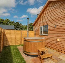 A wooden outdoor hot tub with steps next to a wooden cabin and fenced yard at Peep o Day in Kirkbymoorside