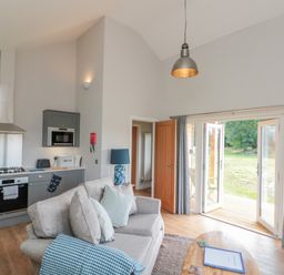 A living room with a gray sofa and kitchen area with gray cabinets and wooden floors at Peep o Day in Kirkbymoorside