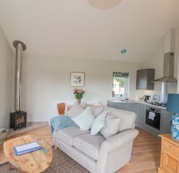 A living room and kitchen area with a gray sofa and wooden coffee table at Peep o Day in Kirkbymoorside