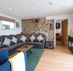 A living room with a leather sectional sofa cushions a wooden coffee table and a stone accent wall at Y Granar in Llanrhaeadr-Ym-Mochnant
