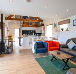 An open plan living room and kitchen with blue and red armchairs a grey sofa a wooden coffee table and a dining table with white chairs at Y Granar Llanrhaeadr-Ym-Mochnant
