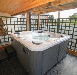 An outdoor covered area with a bubbling hot tub next to a green lattice fence at Y Stabl The Stable in Llanrhaeadr-Ym-Mochnant