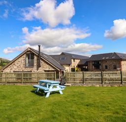 A stone building with a wooden fence and a blue picnic table on green grass at Y Stabl The Stable in Llanrhaeadr-Ym-Mochnant