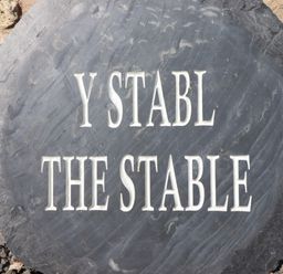 A black stone sign with the text Y Stabl The Stable on a stone wall background at Y Stabl The Stable in Llanrhaeadr-Ym-Mochnant