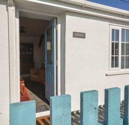 An open door with a blue frame leading into a room with a chair and cabinet behind a blue wooden fence at Ffrwd in Rhosneigr
