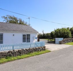 A white house with two windows a light blue fence a stone wall and a driveway gate at Ffrwd in Rhosneigr