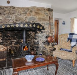 A living room with a stone fireplace wood stove armchair with a blanket and coffee table at Ffrwd in Rhosneigr