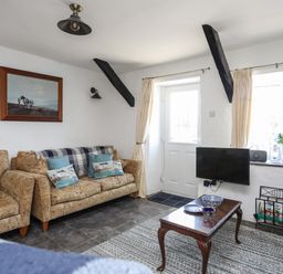 A living room with patterned sofas a wooden coffee table a wall mounted TV and a painting at Ffrwd in Rhosneigr