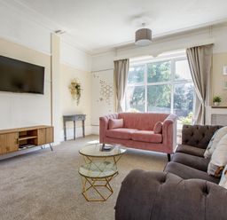 A living room with a pink sofa a grey sofa a wooden TV stand with a TV on the wall and a large window at Sunnymeade in Buxton Norfolk