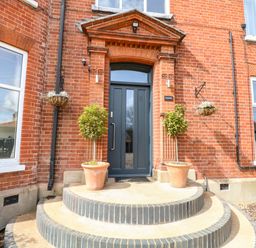 A front entrance with a dark door two potted plants on steps and red brick walls at Sunnymeade in Buxton Norfolk