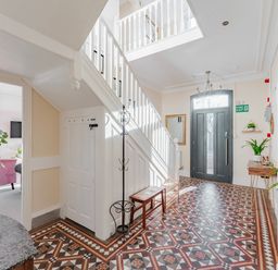 An entrance hallway with tiled floor a dark front door a staircase with white balustrades and various plants at Sunnymeade in Buxton Norfolk