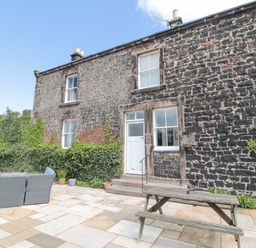 An outdoor patio area with stone paving furniture and a wooden picnic table outside a stone house with ivy growing on the walls at Jubilee House in Embleton