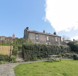 An outdoor garden area with grass a wooden picnic table stone steps leading up to a stone house with ivy on the walls at Jubilee House in Embleton