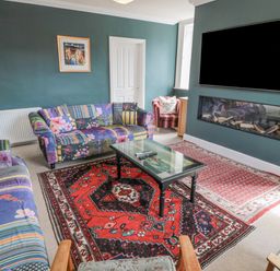 A living room with patterned sofas a glass coffee table a wall-mounted TV and a fireplace at Jubilee House in Embleton