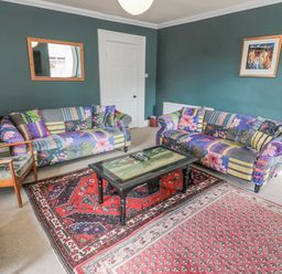 A living room with two patterned sofas a wooden armchair a coffee table and two rugs at Jubilee House in Embleton
